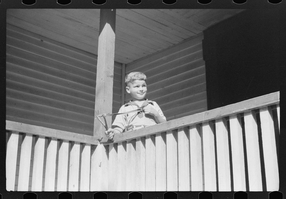 Mountain child shooting slingshot from porch of his home. Near Buckhorn, Kentucky. Sourced from the Library of Congress.