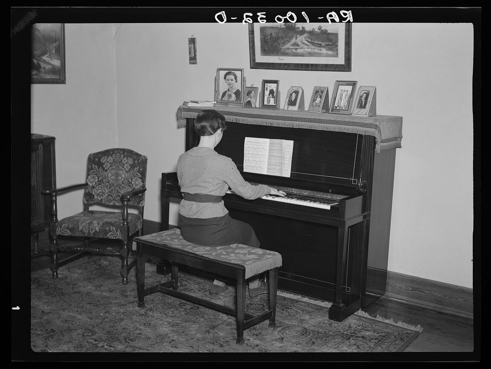 Lois Madsen playing the piano in the home of her father, Harry Madsen, owner-operator of three hundred and sixty acre farm…