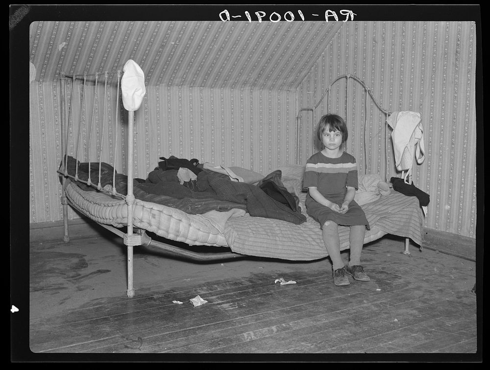 One of Edgar Allen's children sitting on the bed in the house on his farm. There are no sheets, pillowcases, or pillows…