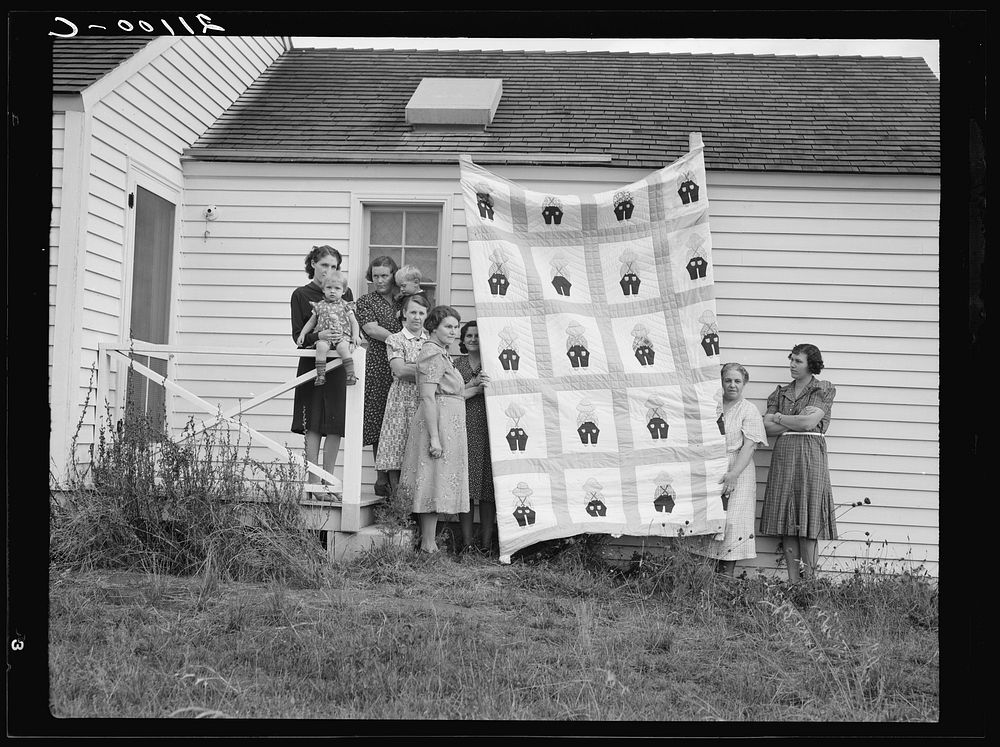 Farm women of the "Helping Hand" club display a pieced quilt which they are making for the benefit of one of their numbers.…