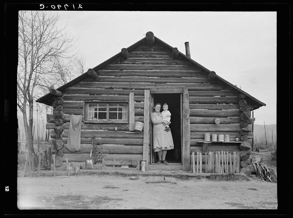 Log house now occupied and enlarged by the Halley family. Mrs. Halley in doorway with youngest child. Bonner County, Idaho.…