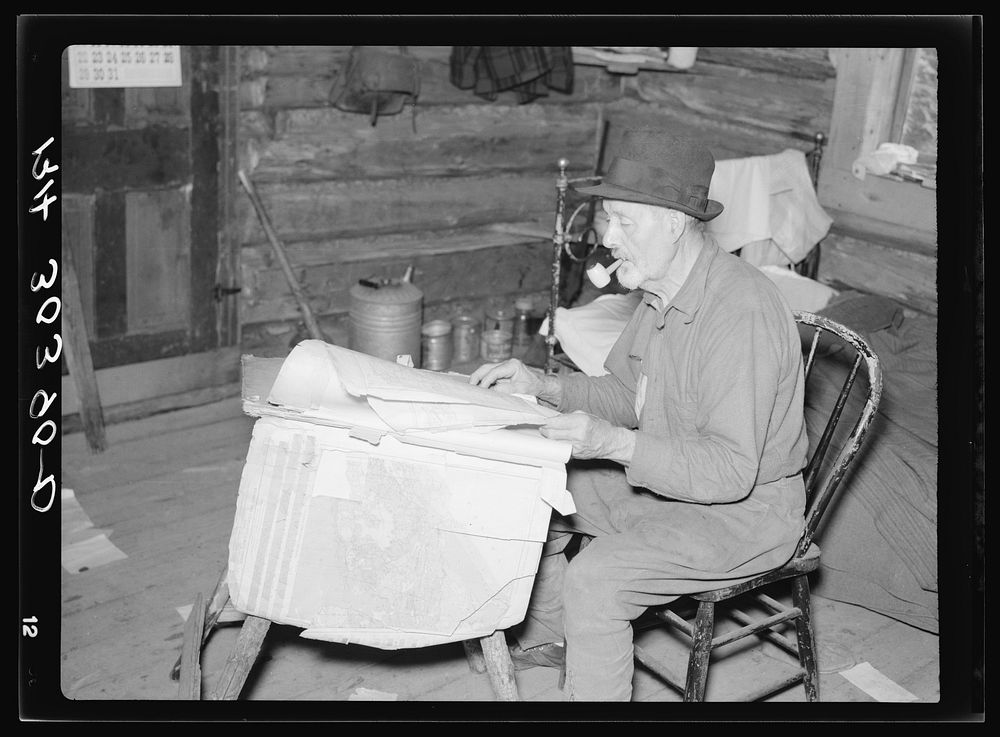 William Besson, iron ore prospector, examining geological survey maps in his cabin near Winton, Minnesota by Russell Lee