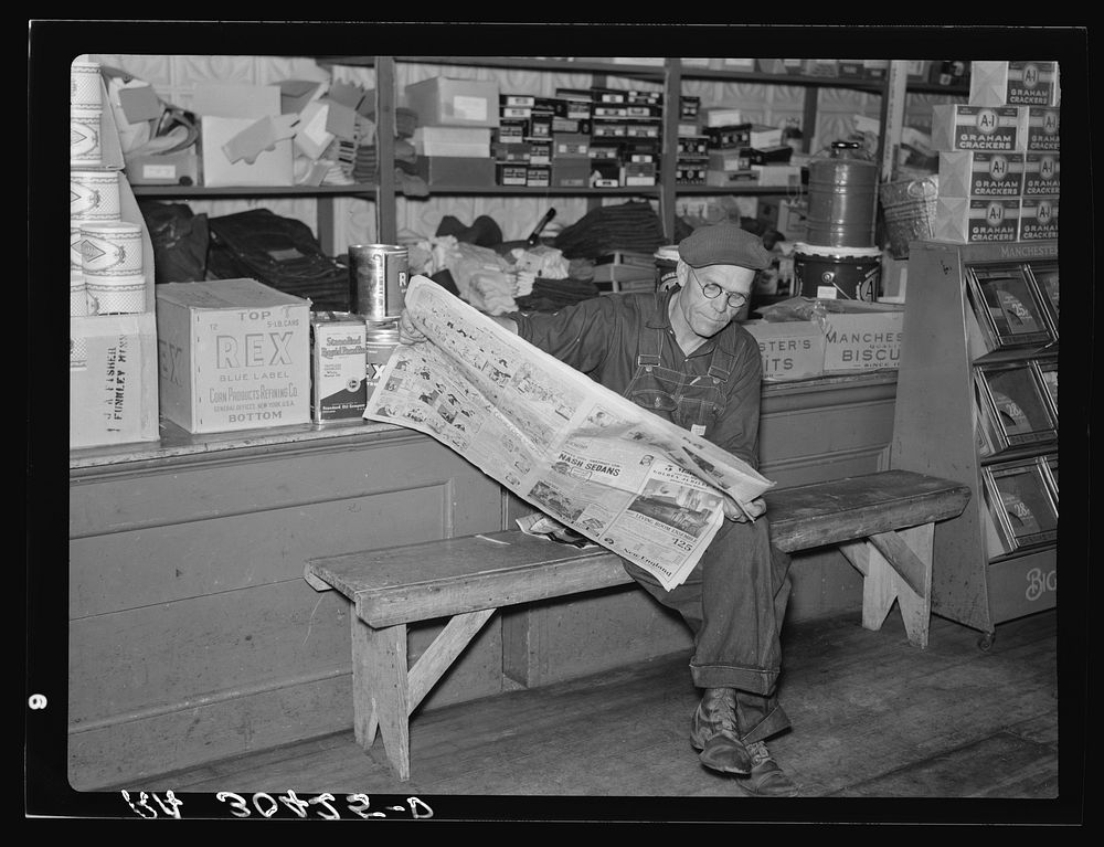 Resident of Funkley, Minnesota, reading newspaper in general store by Russell Lee