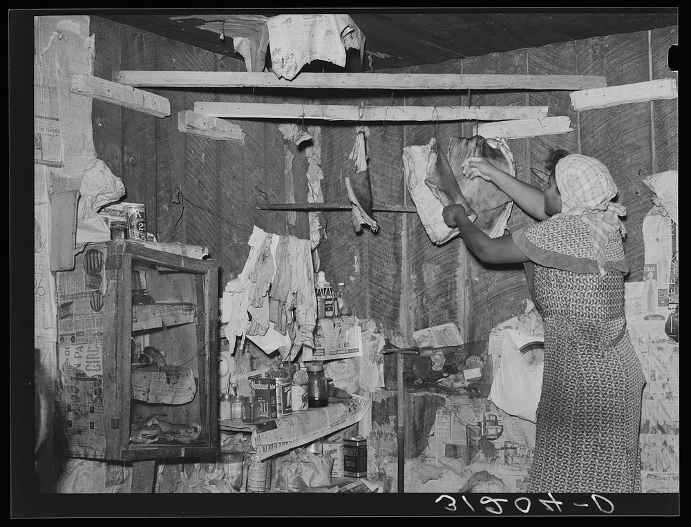 New Madrid County, Missouri. Wife of sharecropper removing fatback from hook in corner of kitchen by Russell Lee