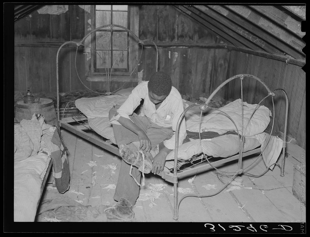 New Madrid County, Missouri. Son of sharecropper putting on shoes in attic bedroom of his home by Russell Lee