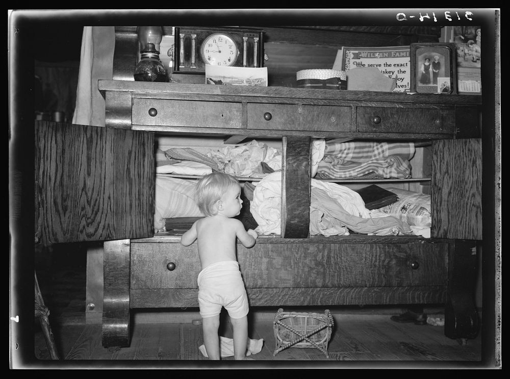 Child playing in front of bureau stuffed with blankets and clothing. Tin Town, Caruthersville, Missouri by Russell Lee