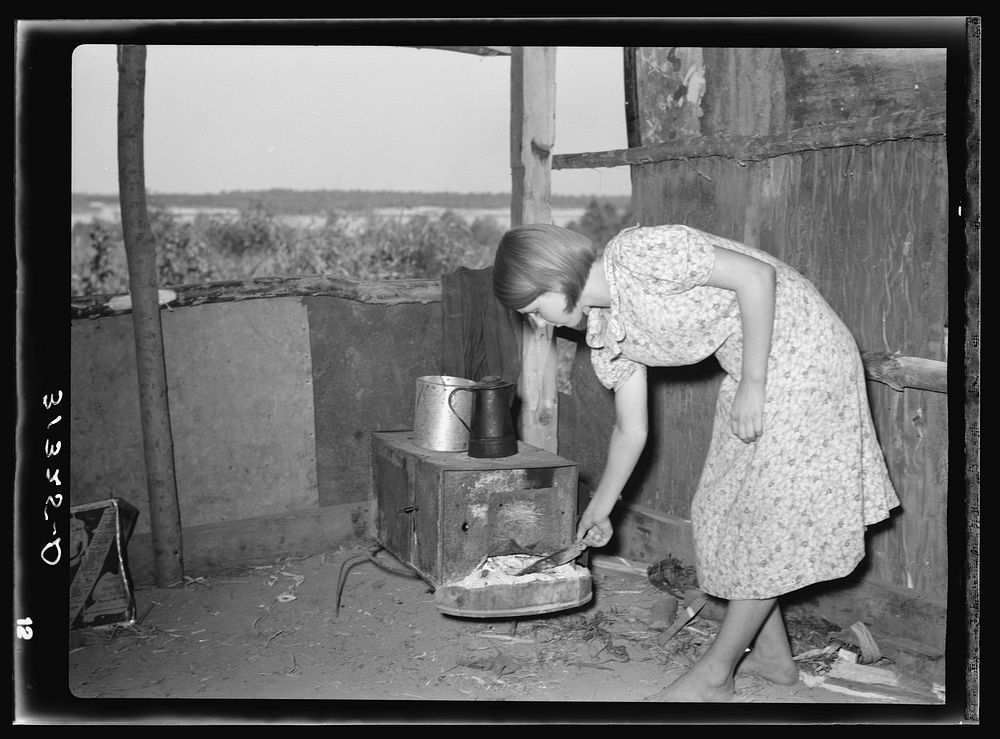 Girl tending fire in shack home. Tin Town, Caruthersville, Missouri by Russell Lee