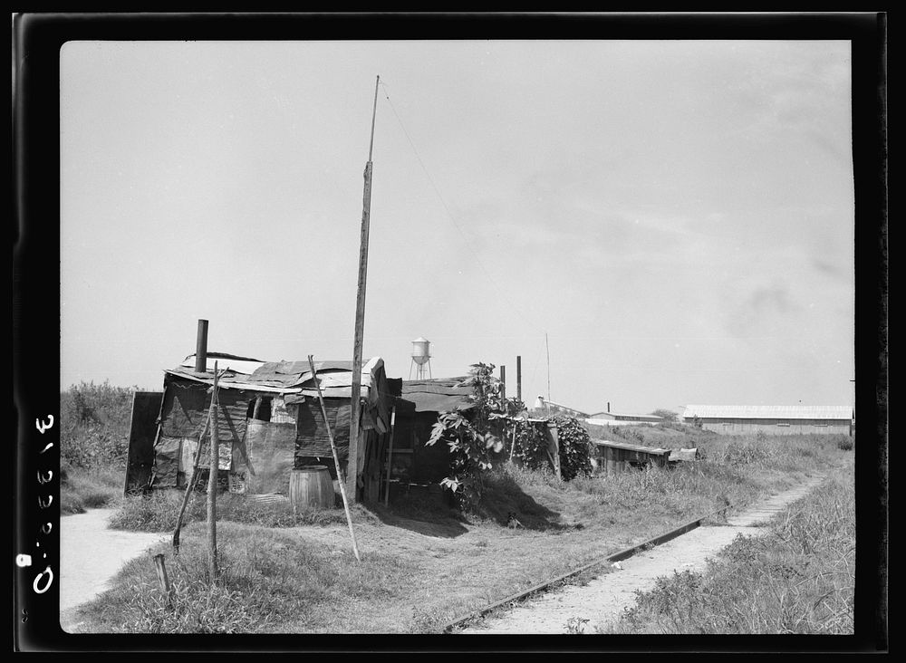 Line of shacks in Tin Town, Caruthersville, Missouri. Industrial plant in the background by Russell Lee