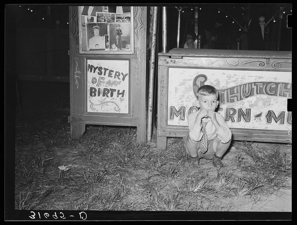 Boy squatting in front of concession. South Louisiana State Fair, Donaldsonville, Louisiana by Russell Lee
