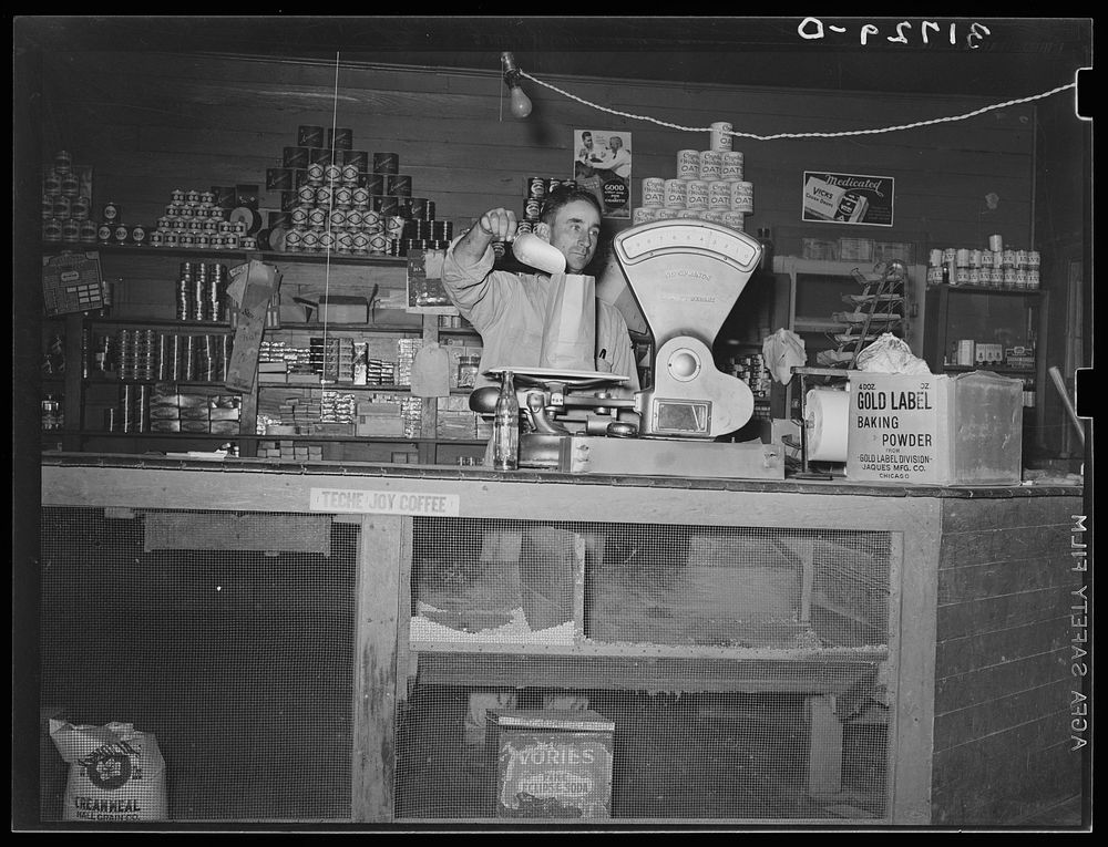 Proprietor of small grocery store weighing dried beans. Near New Iberia, Louisiana. This small grocery store was the center…