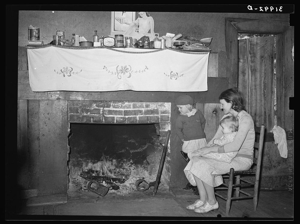 Mrs. Bagget and two children in front of fireplace. Note the board window. Laurel, Mississippi by Russell Lee