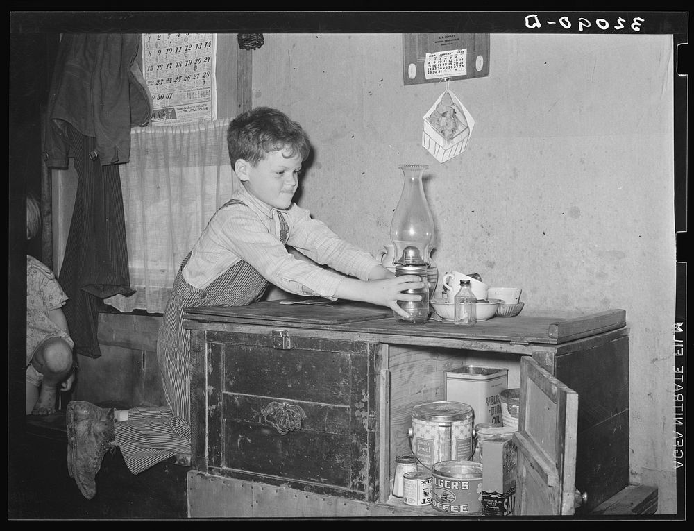 Son of migrant worker reaching for lamp atop cabinet in trailer home. Weslaco, Texas. See caption 32108-D by Russell Lee