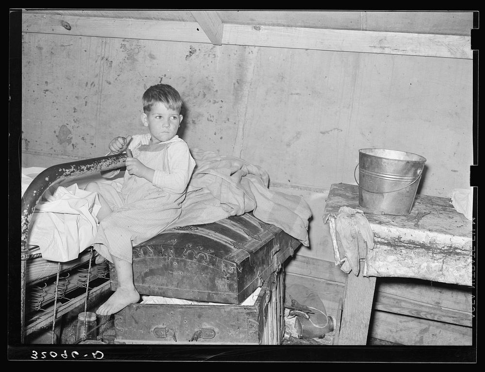 Son of white migrants sitting on trunk in tent home. Weslaco, Texas. See caption 32108-D by Russell Lee
