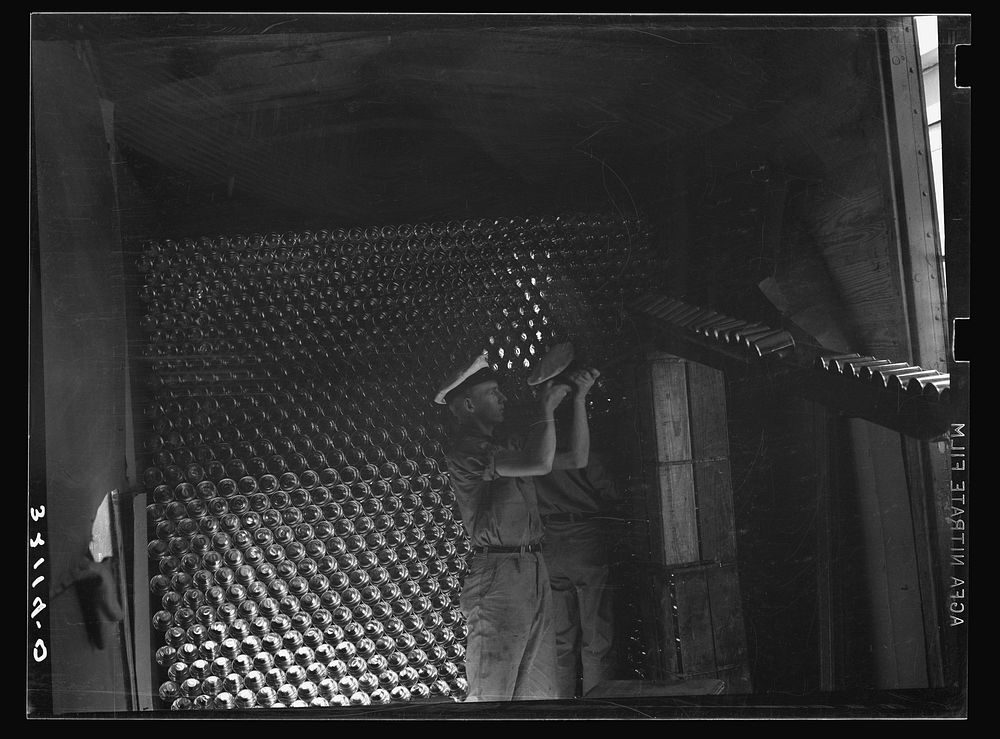 [Untitled photo, possibly related to: Unloading cans from a boxcar is done by picking them up on a row of spikes placed on a…