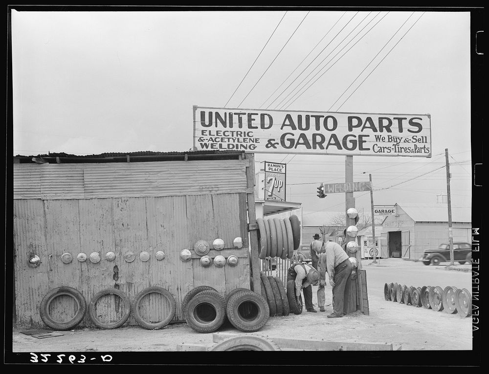 Secondhand automobile parts and garage with customer examining secondhand casing. Corpus Christi, Texas. All Mexicans are…