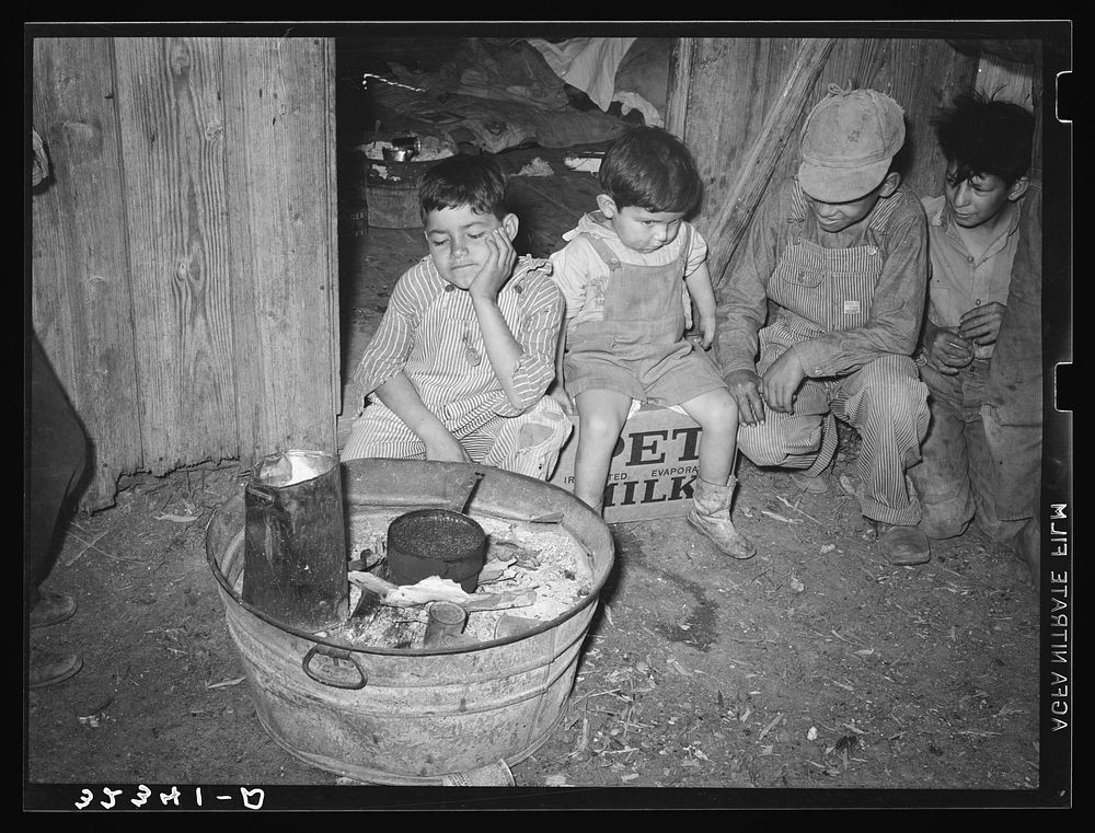 Mexican children sitting outside of corral before fire built in wash tub. Robstown, Texas by Russell Lee