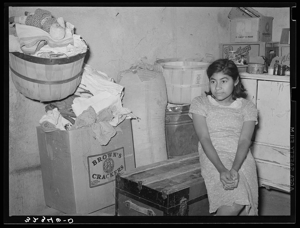Mexican girl sitting in corner of combined living room and kitchen. Crystal City, Texas by Russell Lee