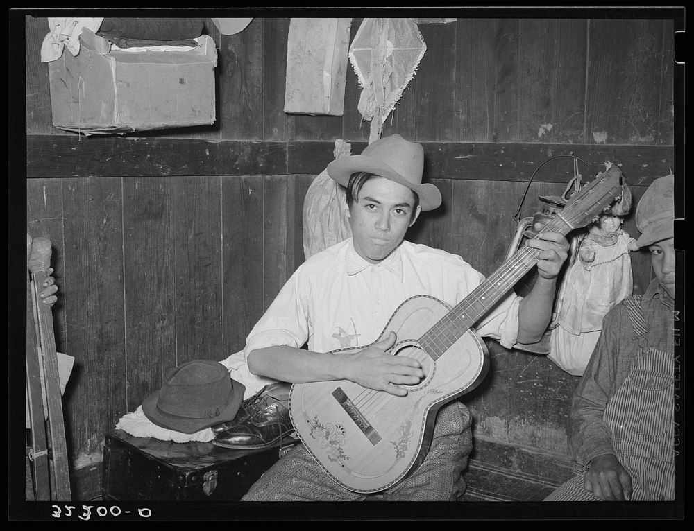Mexican boy playing guitar in room of corral. Robstown, Texas by Russell Lee