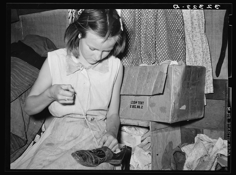 Daughter of white migrants repairing shoes with cotton thread. Sebastian, Texas by Russell Lee