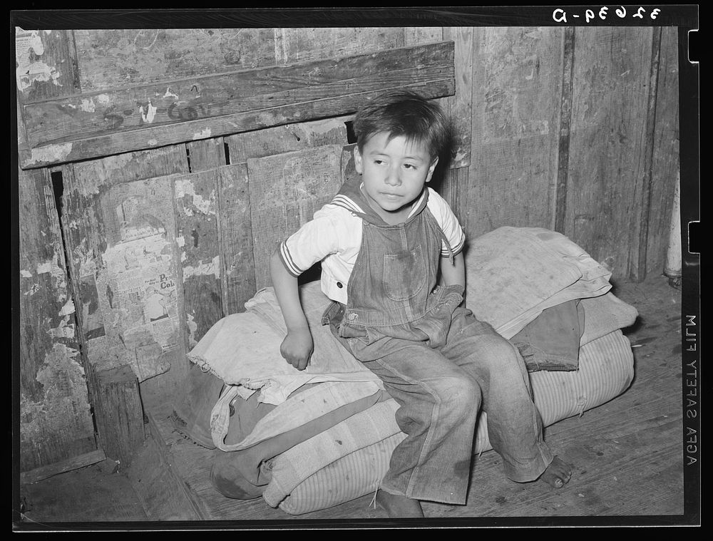 Mexican boy sitting on bedroll. These rolls are used on the floor for beds at night, rolled up during the day. San Antonio…