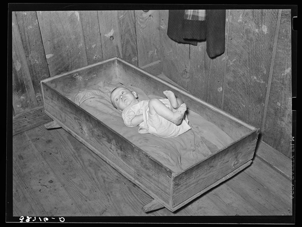 Baby of family living on relief. Notice the homemade cradle. Near Jefferson, Texas. Housing conditions in this section are…