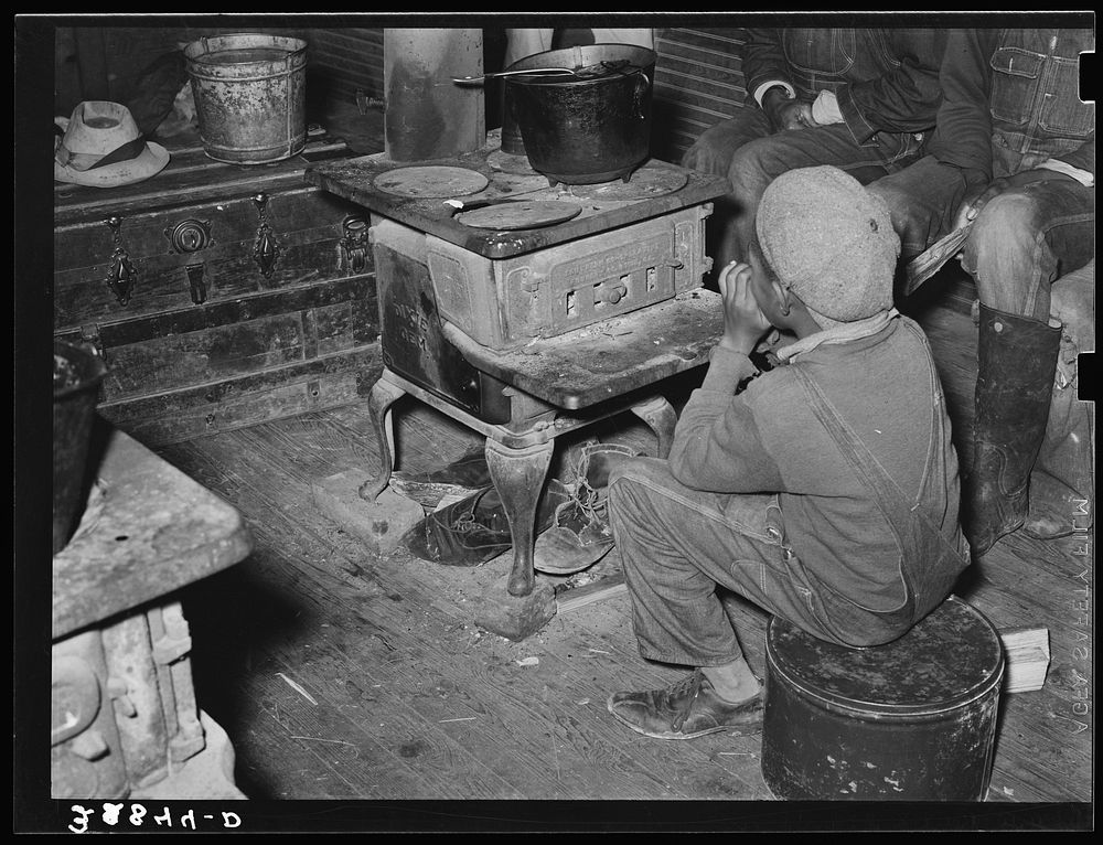 Boy sitting by the stove on a cold day in the strawberry picking season. Near Independence, Louisiana by Russell Lee
