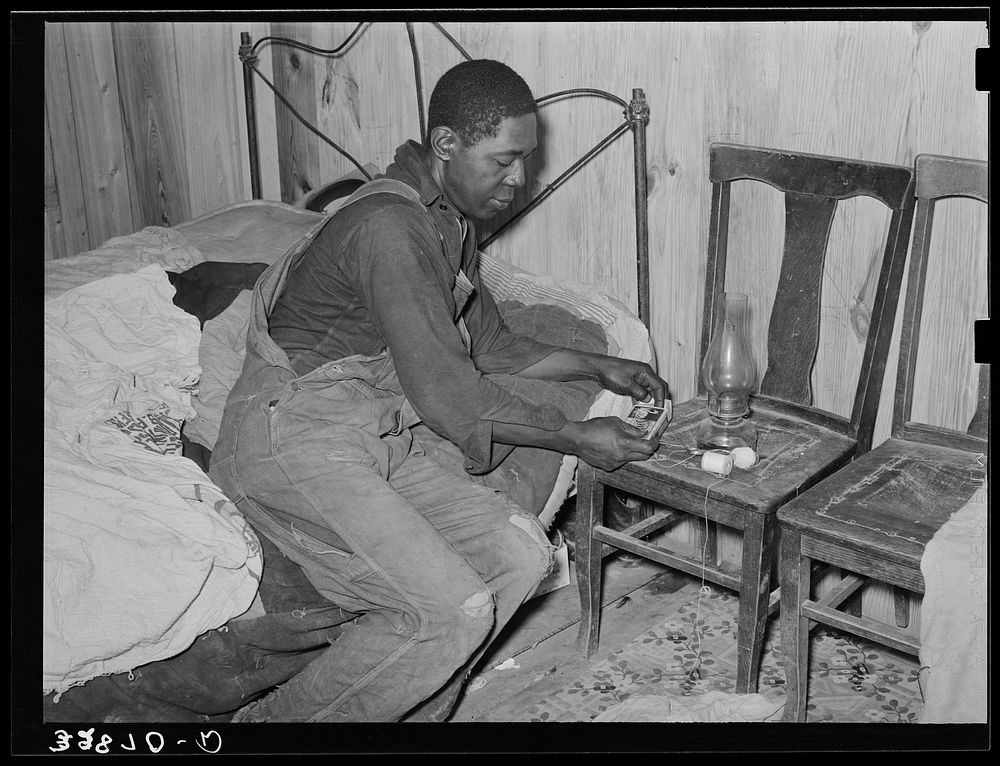  man lighting lamp in bedroom of his home near Hammond, Louisiana. He works for a strawberry grower, doing odd jobs about…