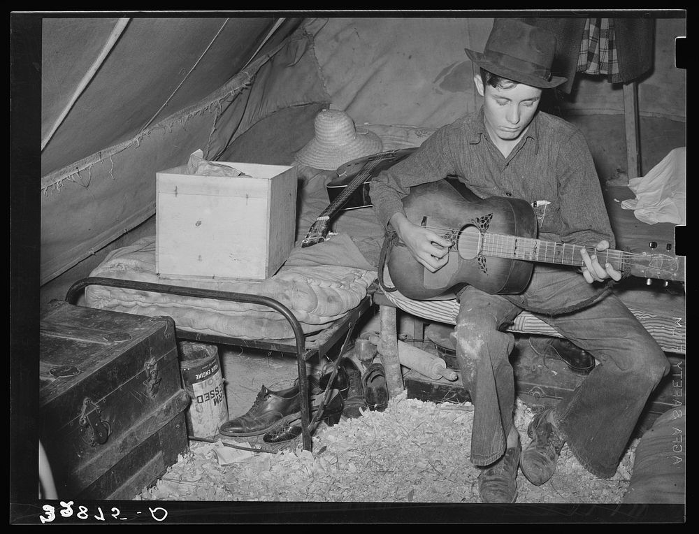 White migrant strawberry picker playing guitar in his tent near Hammond, Louisiana by Russell Lee