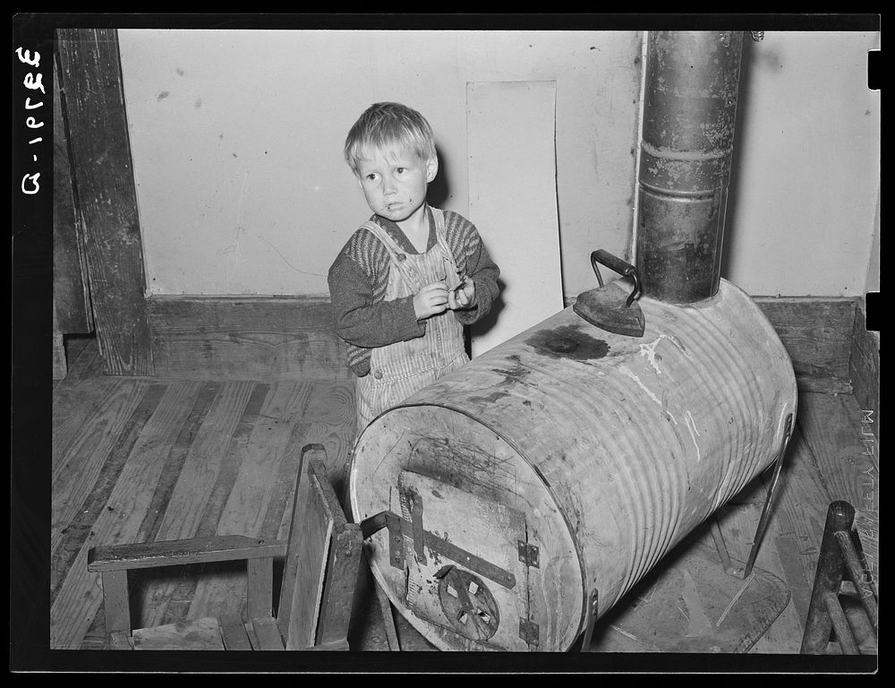 Child of relief family standing by stove made of oil drum. Near Jefferson, Texas by Russell Lee
