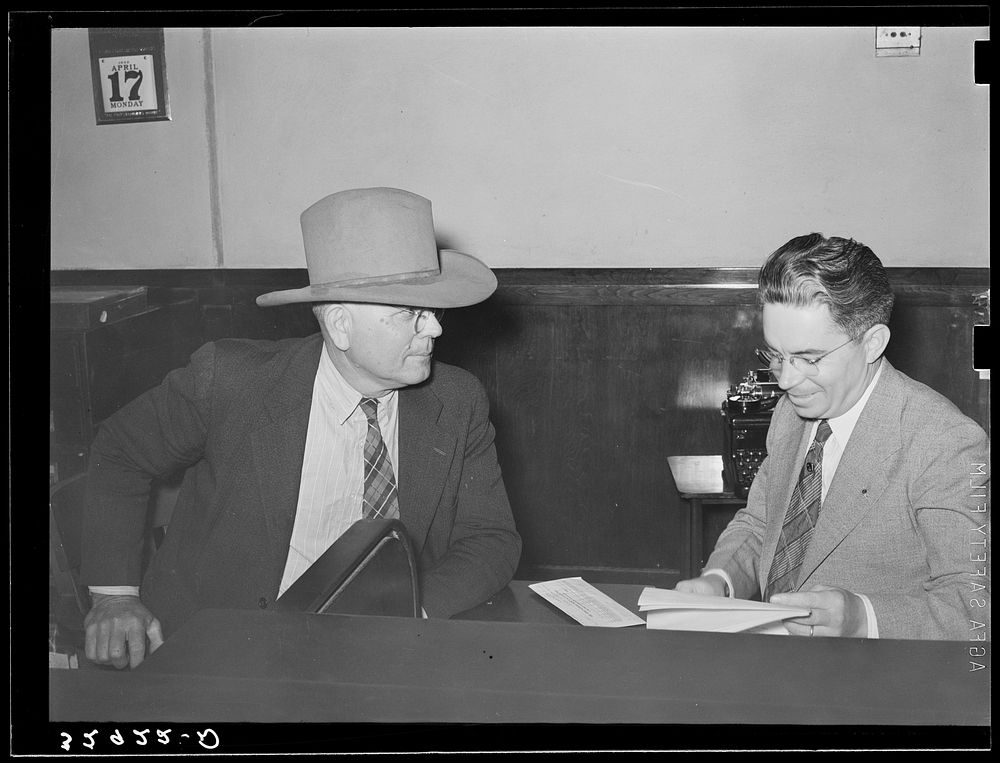 Sheriff of adjoining county talking to cashier in bank. San Augustine, Texas by Russell Lee