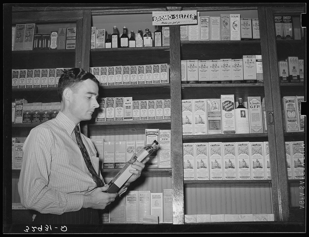 Druggist in front of patent medicine shelf. San Augustine, Texas by Russell Lee