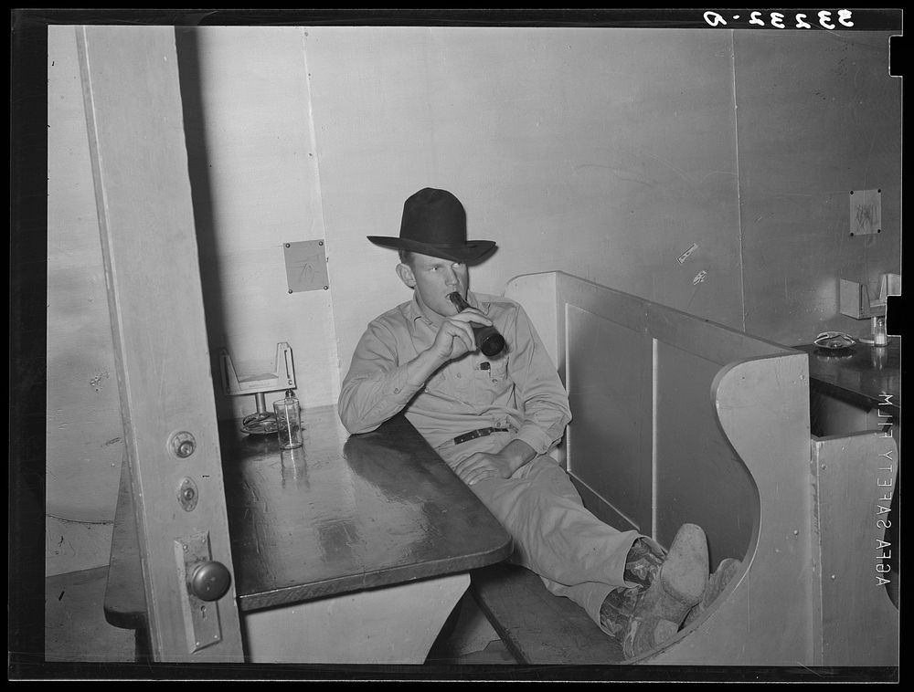 Cowboy drinking a bottle of beer in booth of beer parlor. Alpine, Texas by Russell Lee