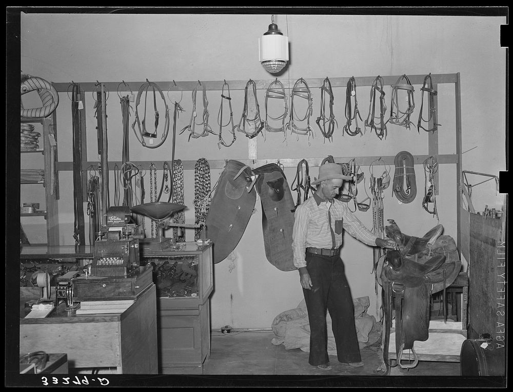 Cowboy examining saddle. Ranch supply store, Alpine, Texas by Russell Lee
