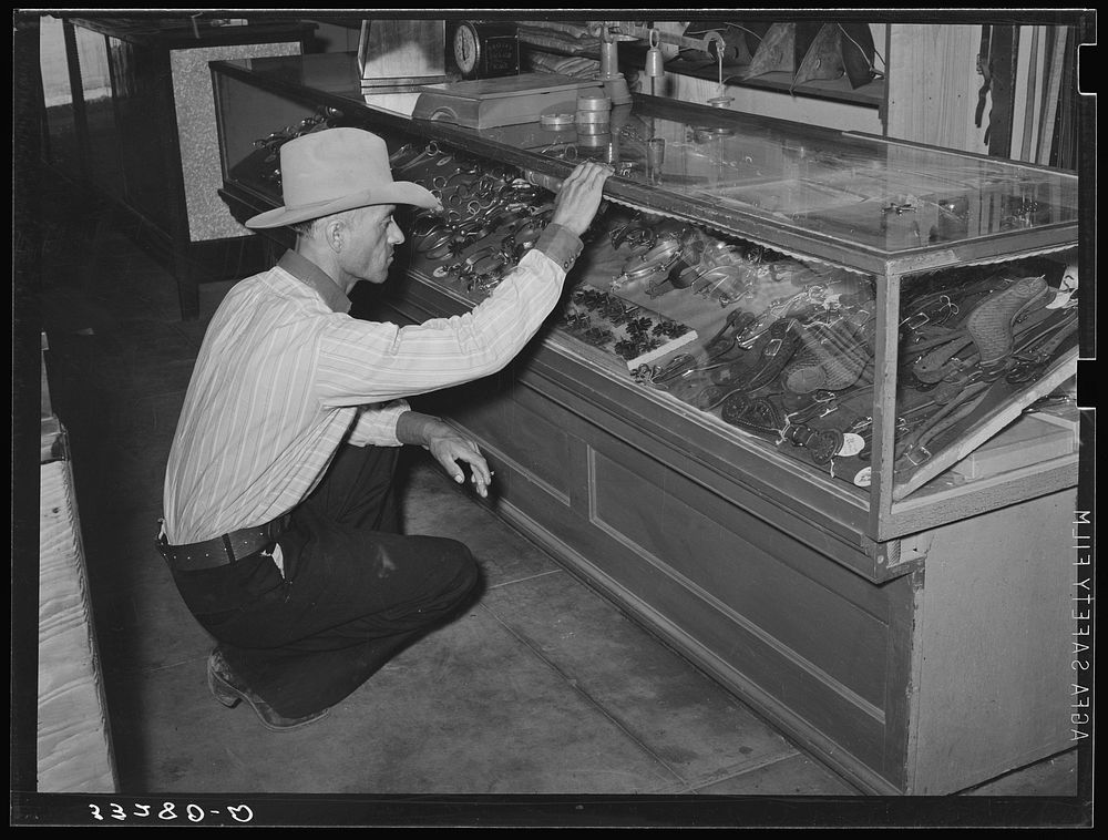 Cowboy looking at display of spurs. Ranch supply store, Alpine, Texas by Russell Lee