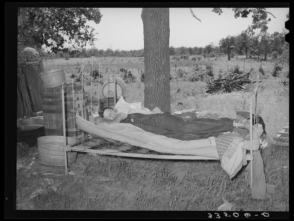 Young migrant agricultural worker on bed outside his home in McIntosh County, Oklahoma by Russell Lee