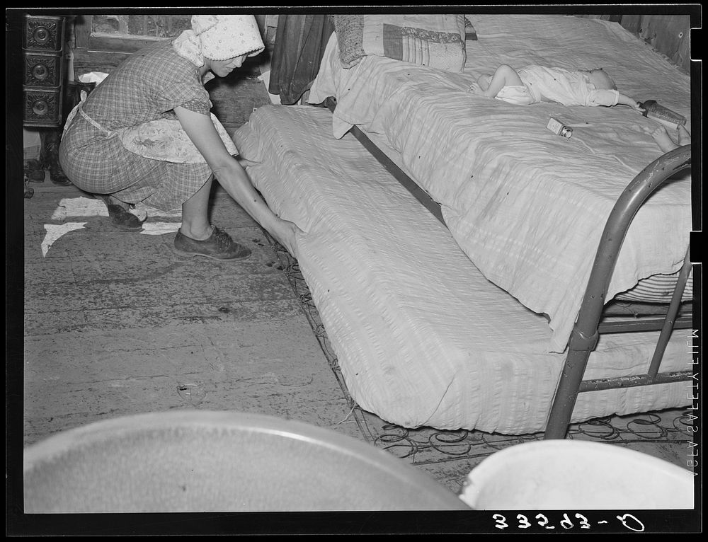 Wife of tenant farmer pulling out trundle bed in her one-room shack home near Sallisaw, Okahoma by Russell Lee