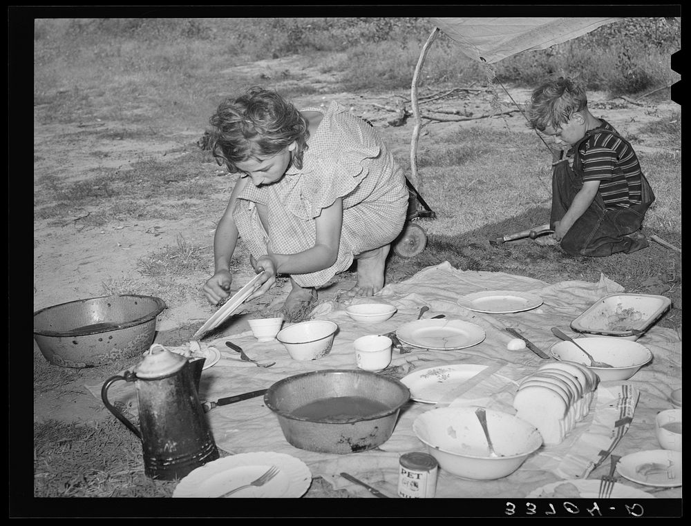 Migrant girl scraping plates after noonday meal along the highway near Muskogee, Oklahoma. Muskogee County by Russell Lee