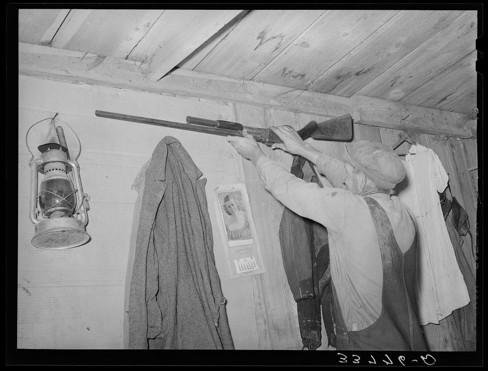 Moving the rifle which was placed on the wall before leaving for California from Muskogee, Oklahoma by Russell Lee