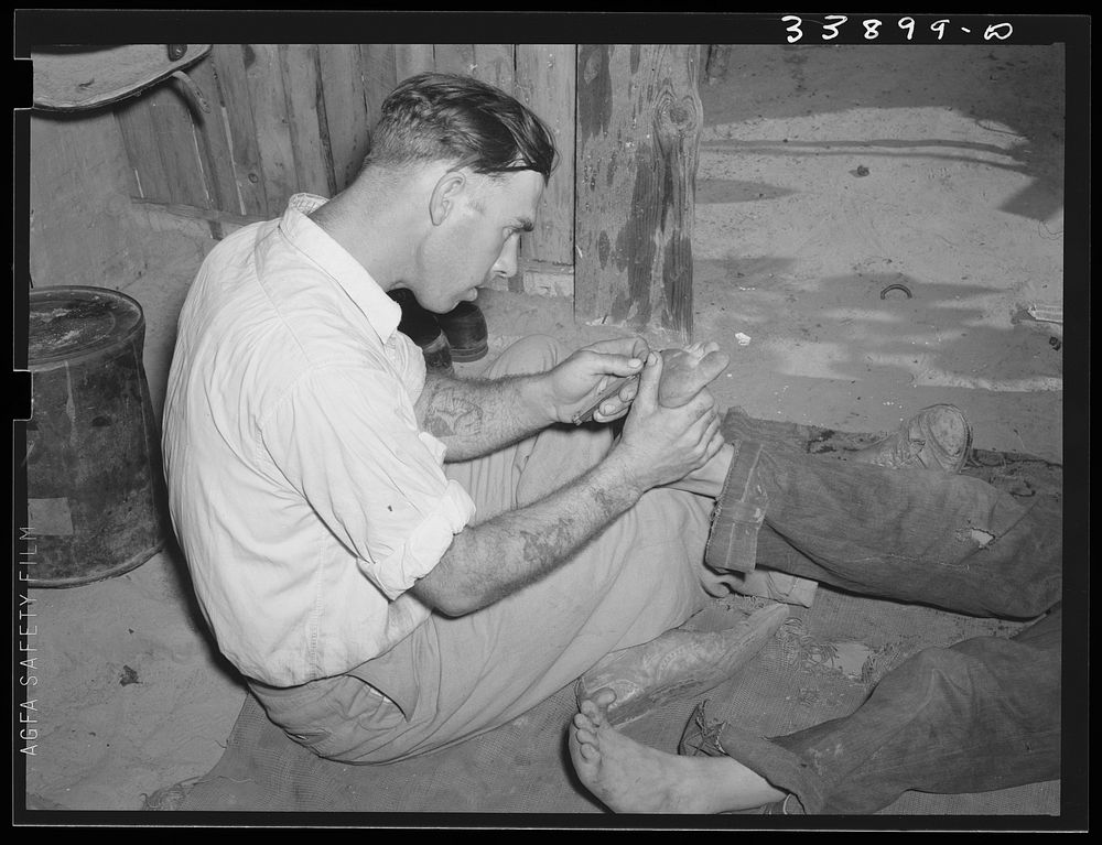 Resident of Mays Avenue camp taking out a piece of glass from boy's foot. Oklahoma City, Oklahoma by Russell Lee
