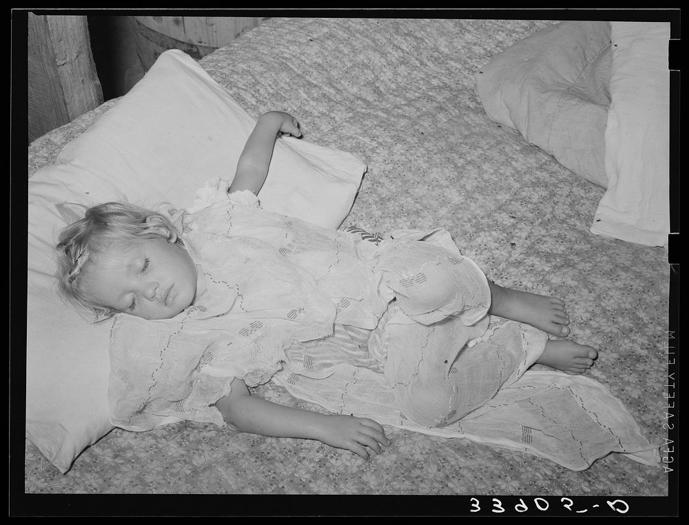 Daughter of water peddler in community camp, Oklahoma City, Oklahoma, asleep. She is covered with old curtain to protect her…