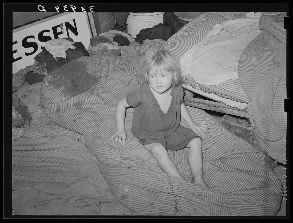 Child of large family sitting on bedding in shack home. Mays Avenue camp, Oklahoma City, Oklahoma by Russell Lee