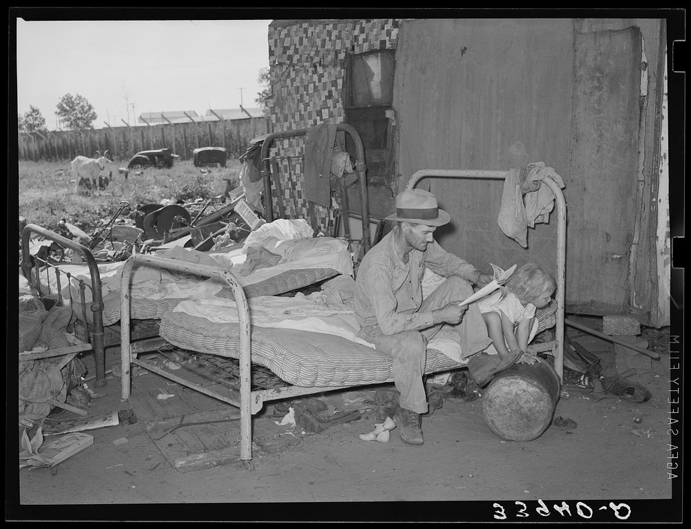 Man with his daughter sitting on bed which is outdoors under bridge in Mays Avenue camp. Oklahoma City, Oklahoma by Russell…