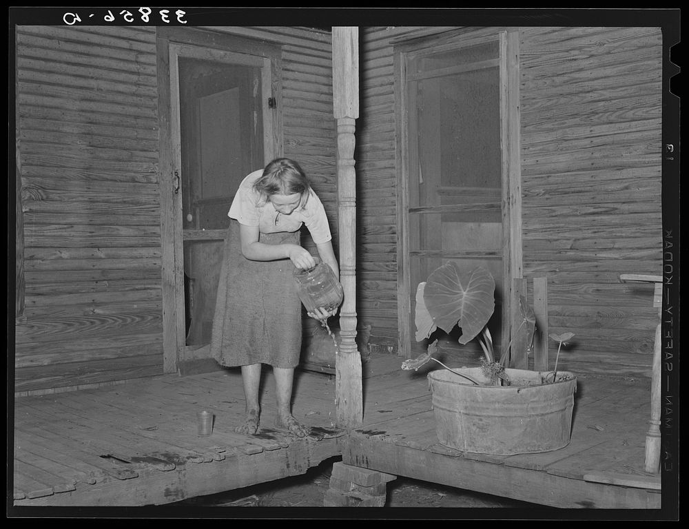 Front porch of tenant farmer's house near Muskogee, Oklahoma. Daughter is getting ready to change water in goldfish bowl.…