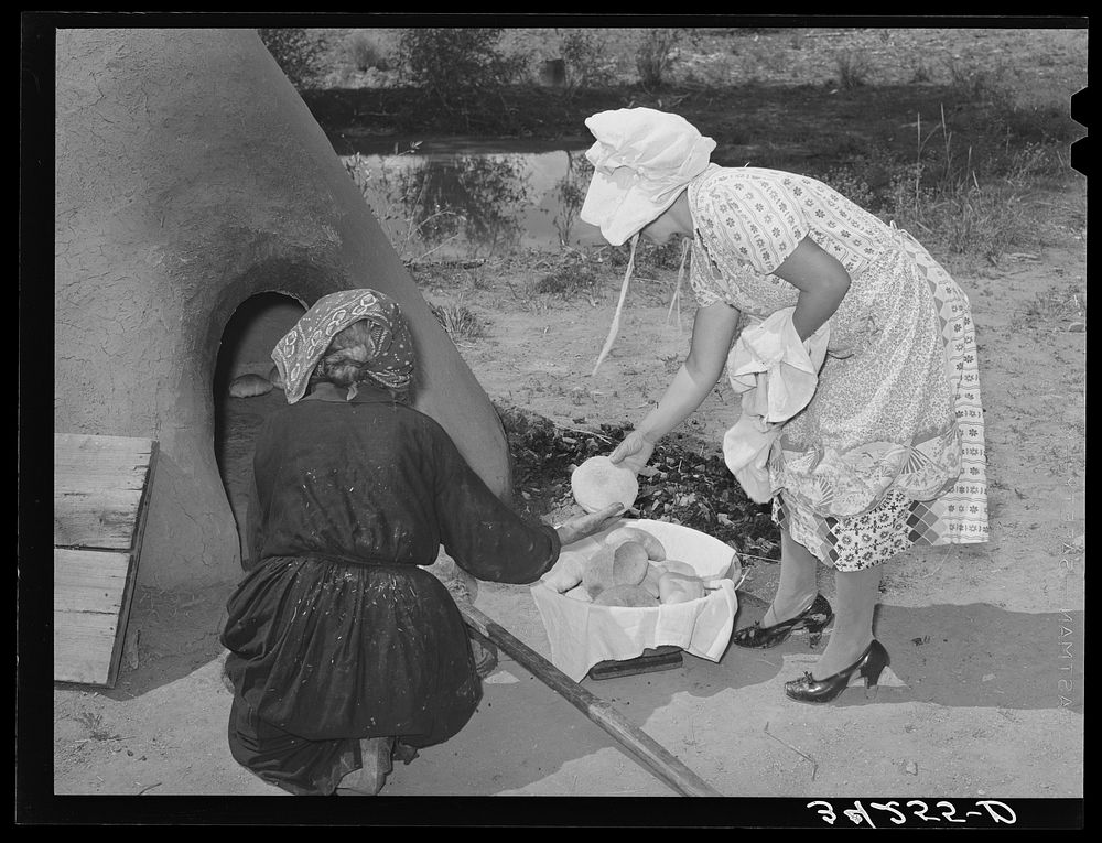 Wiping ashes from freshly-baked bread which has just been removed from earthen oven. Spanish-American farm home near Taos…
