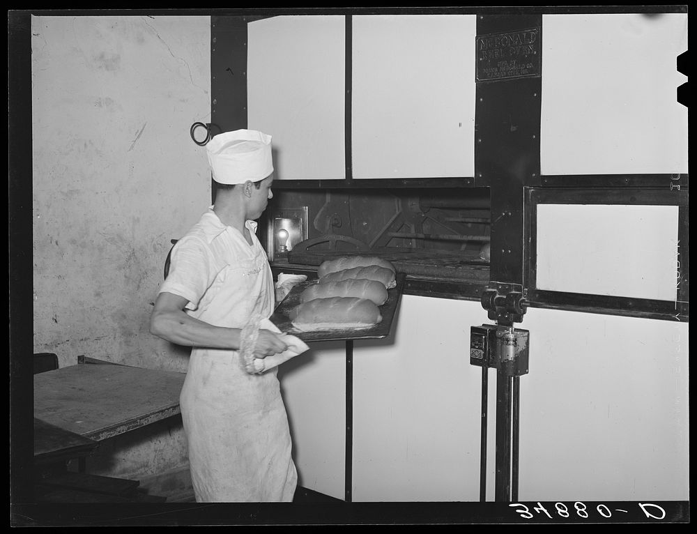 Removing tray of freshly baked bread from conveyor type oven. Bakery, San Angelo, Texas by Russell Lee