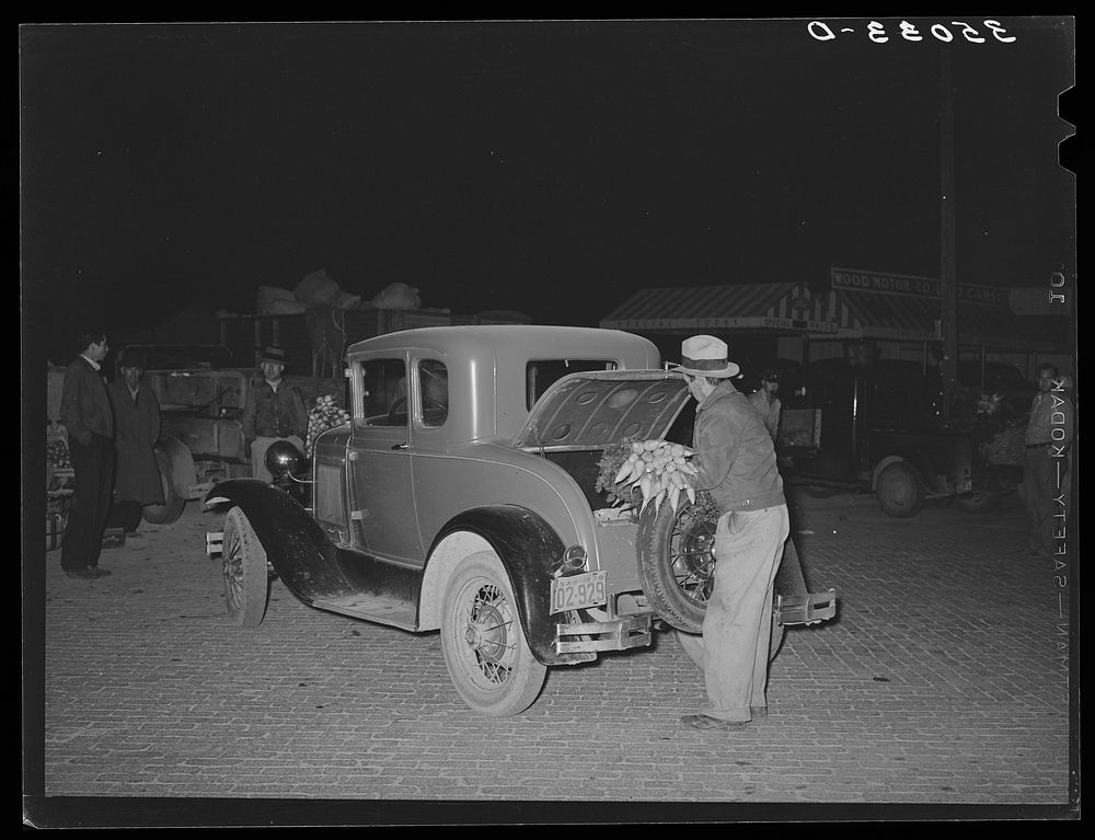 Farmer putting vegetables in rear of car at early morning vegetable market. San Angelo, Texas by Russell Lee