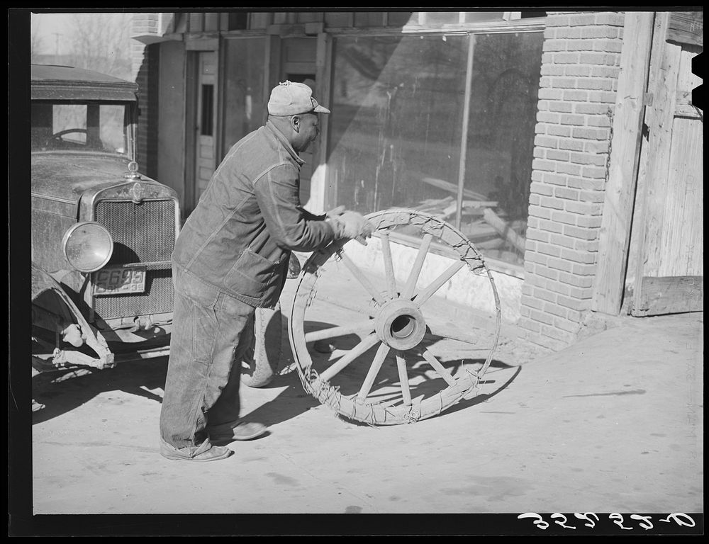  farmer rolling much-repaired wagon wheel into smith shop to see if it can again be repaired. Depew, Oklahoma by Russell Lee