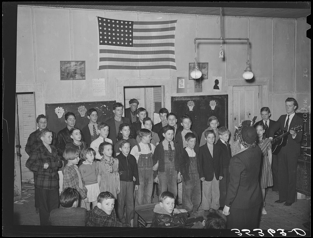 Schoolchildren, directed by their music teacher, sing at the pie supper. McIntosh County, Oklahoma. See general caption…