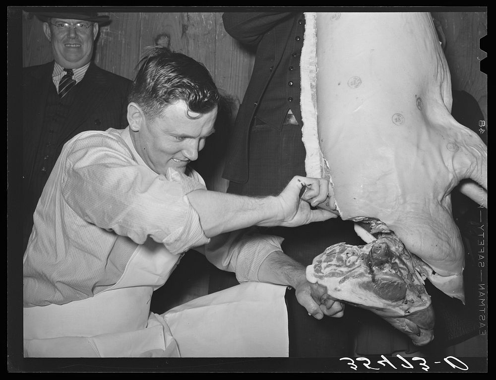 FSA (Farm Security Administration) supervisor giving a demonstration of meat cutting before a group of FSA officials at a…