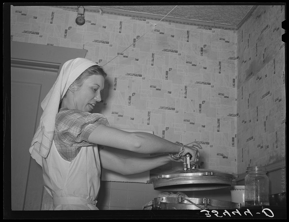 FSA (Farm Security Administration) supervisor removing the top pressure cooker during a demonstration of pressure canning…